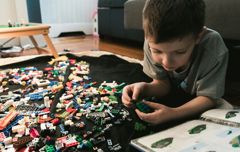 Boy playing with LEGO A child lying on the floor, focused on building with colorful Lego blocks scattered around, with an instruction booklet next to them.
